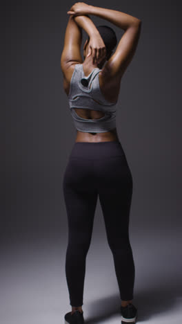 Vertical-Video-Rear-View-Studio-Shot-Of-Woman-Wearing-Gym-Fitness-Clothing-Doing-Warm-Up-Exercises-And-Stretching